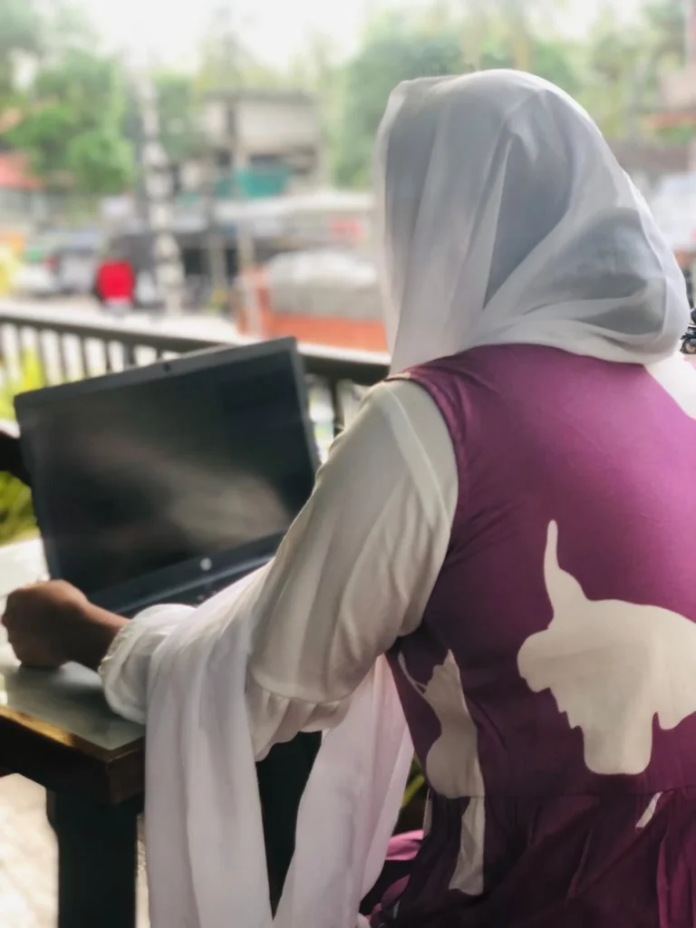"Leading top digital marketing freelancer in Calicut, a Muslim woman in hijab working on a laptop at an outdoor café with a street view in the background."